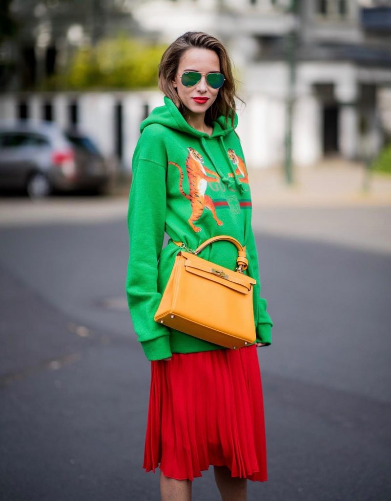 Alexandra Lapp in a Hermès Kelly Look wearing a green tiger print Gucci logo hoodie, a red pleated skirt by SET, a Hermes Birkin 30 bag in orange, Pigalle Follies pumps by Christian Louboutin and green mirrored Ray Ban sunglasses on May 3, 2018 in Duesseldorf, Germany. 