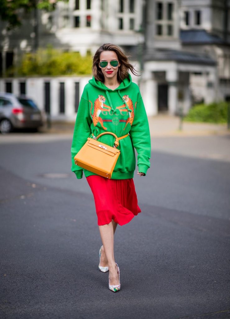 Alexandra Lapp in a Hermès Kelly Look wearing a green tiger print Gucci logo hoodie, a red pleated skirt by SET, a Hermes Birkin 30 bag in orange, Pigalle Follies pumps by Christian Louboutin and green mirrored Ray Ban sunglasses on May 3, 2018 in Duesseldorf, Germany. 