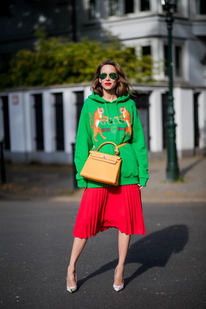 Alexandra Lapp in a Hermès Kelly Look wearing a green tiger print Gucci logo hoodie, a red pleated skirt by SET, a Hermes Birkin 30 bag in orange, Pigalle Follies pumps by Christian Louboutin and green mirrored Ray Ban sunglasses on May 3, 2018 in Duesseldorf, Germany. 