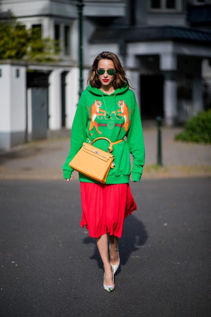 Alexandra Lapp in a Hermès Kelly Look wearing a green tiger print Gucci logo hoodie, a red pleated skirt by SET, a Hermes Birkin 30 bag in orange, Pigalle Follies pumps by Christian Louboutin and green mirrored Ray Ban sunglasses on May 3, 2018 in Duesseldorf, Germany. 