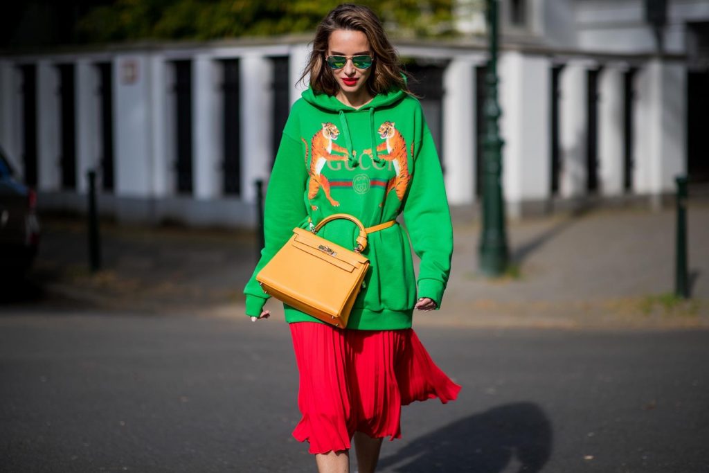 Alexandra Lapp in a Hermès Kelly Look wearing a green tiger print Gucci logo hoodie, a red pleated skirt by SET, a Hermes Birkin 30 bag in orange, Pigalle Follies pumps by Christian Louboutin and green mirrored Ray Ban sunglasses on May 3, 2018 in Duesseldorf, Germany. 