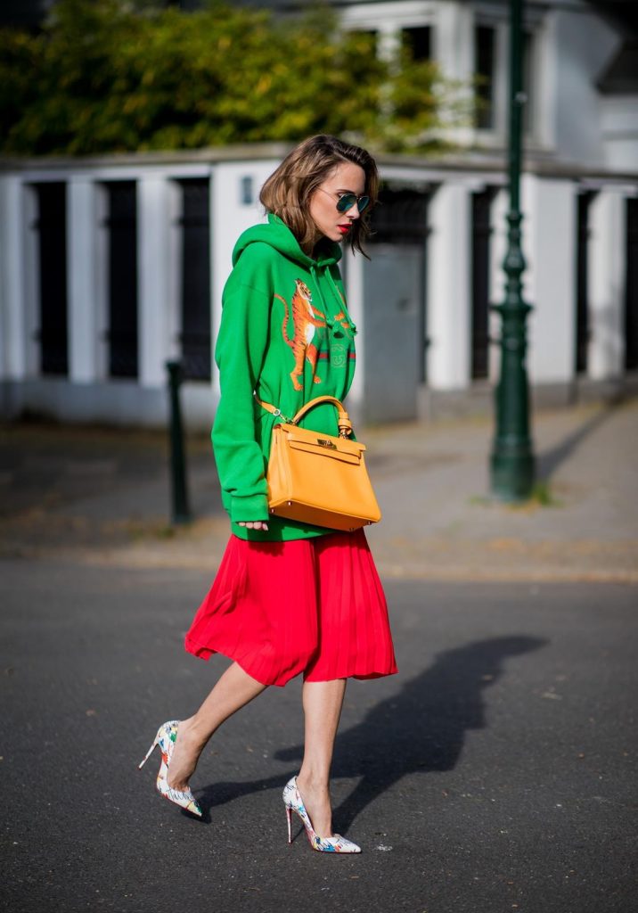 Alexandra Lapp in a Hermès Kelly Look wearing a green tiger print Gucci logo hoodie, a red pleated skirt by SET, a Hermes Birkin 30 bag in orange, Pigalle Follies pumps by Christian Louboutin and green mirrored Ray Ban sunglasses on May 3, 2018 in Duesseldorf, Germany. 