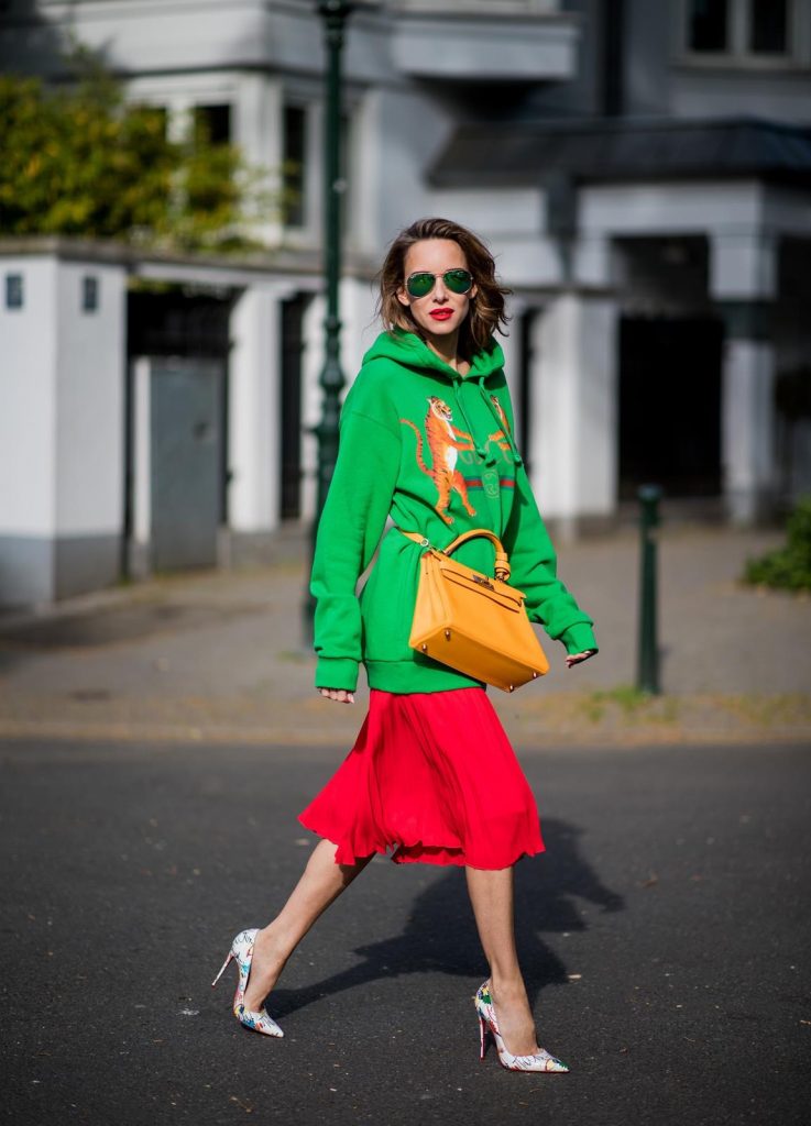 Alexandra Lapp in a Hermès Kelly Look wearing a green tiger print Gucci logo hoodie, a red pleated skirt by SET, a Hermes Birkin 30 bag in orange, Pigalle Follies pumps by Christian Louboutin and green mirrored Ray Ban sunglasses on May 3, 2018 in Duesseldorf, Germany. 