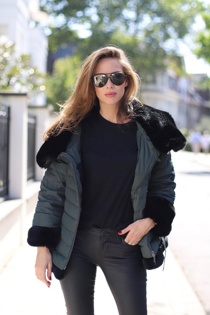 Model and Blogger Alexandra Lapp in a Faux Fur Jacket Look wearing a black down jacket with faux fur by Airfield, black leather pants by SET, black T-Shirt by James Perse, dark green leather overknee boots by Saint Laurent, black Kelly bag by Hermès and black Audrey sunglasses from Céline.