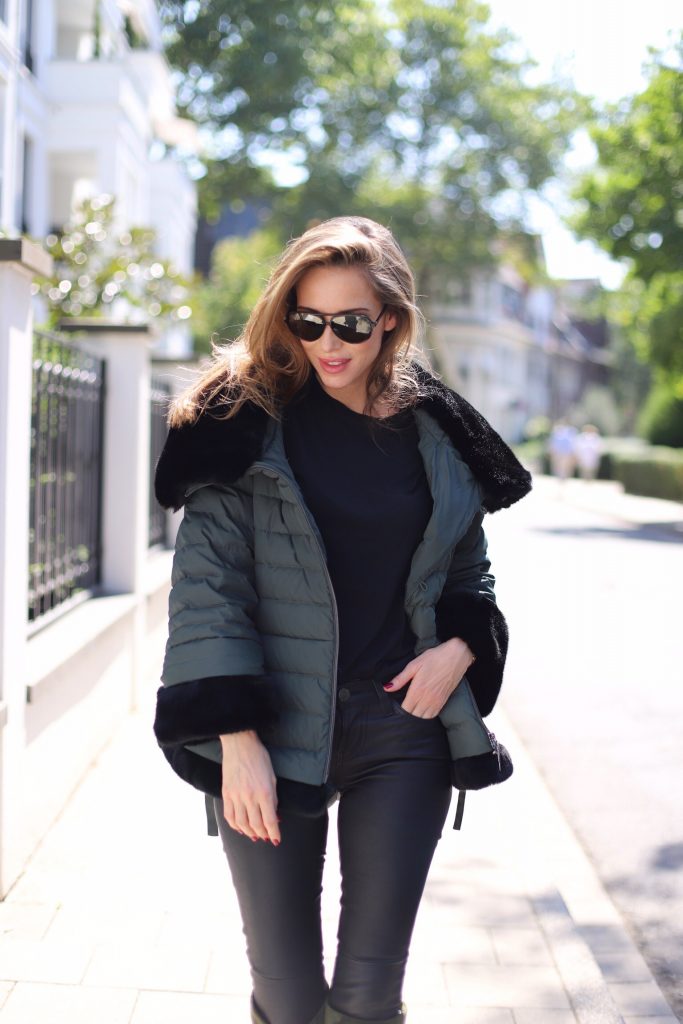 Model and Blogger Alexandra Lapp in a Faux Fur Jacket Look wearing a black down jacket with faux fur by Airfield, black leather pants by SET, black T-Shirt by James Perse, dark green leather overknee boots by Saint Laurent, black Kelly bag by Hermès and black Audrey sunglasses from Céline.