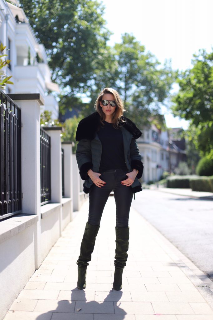  Model and Blogger Alexandra Lapp in a Faux Fur Jacket Look wearing a black down jacket with faux fur by Airfield, black leather pants by SET, black T-Shirt by James Perse, dark green leather overknee boots by Saint Laurent, black Kelly bag by Hermès and black Audrey sunglasses from Céline.