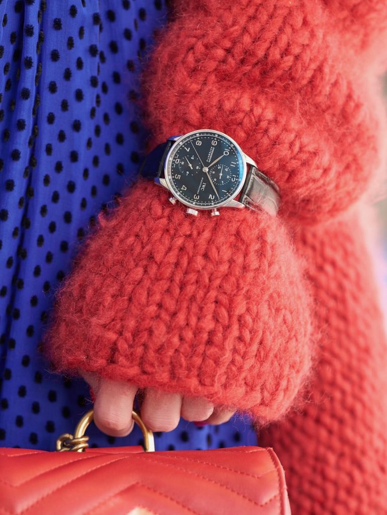 Model and blogger Alexandra Lapp with IWC Watches wearing a blue Polka-dot silk-blend dress by Valentino, Elado Cashmere and Silk-blend Cardigan in red by The Row, red Gg Marmont Quilted Leather Backpack by Gucci, red Céline Cat-Eye Sunglasses, red Gianvito Rossi heels, IWC Portugieser Chronograph and the Portofino Automatic Limited Edition by IWC.