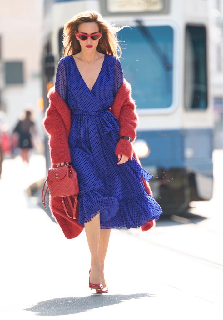 Model and blogger Alexandra Lapp with IWC Watches wearing a blue Polka-dot silk-blend dress by Valentino, Elado Cashmere and Silk-blend Cardigan in red by The Row, red Gg Marmont Quilted Leather Backpack by Gucci, red Céline Cat-Eye Sunglasses, red Gianvito Rossi heels, IWC Portugieser Chronograph and the Portofino Automatic Limited Edition by IWC.