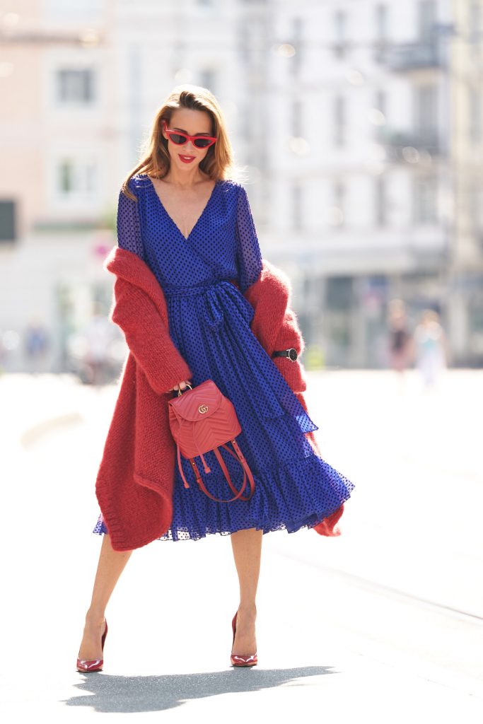 Model and blogger Alexandra Lapp with IWC Watches wearing a blue Polka-dot silk-blend dress by Valentino, Elado Cashmere and Silk-blend Cardigan in red by The Row, red Gg Marmont Quilted Leather Backpack by Gucci, red Céline Cat-Eye Sunglasses, red Gianvito Rossi heels, IWC Portugieser Chronograph and the Portofino Automatic Limited Edition by IWC.