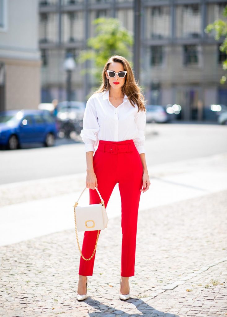 Alexandra Lapp in a Suit Style wearing a red suit combination in bright red with high waist pants with an attached belt and a slim cut blazer with an integrated waist belt, and a white shirt and a short loose knit wool coat in blue, red and white from Steffen Schraut, white snake pumps from Christian Louboutin, white and black cat-eye sunglasses by Saint Laurent and a white handbag from Roger Vivier with a golden buckle and chain seen during the Berlin Fashion Week July 2018 on July 5, 2018 in Berlin, Germany.