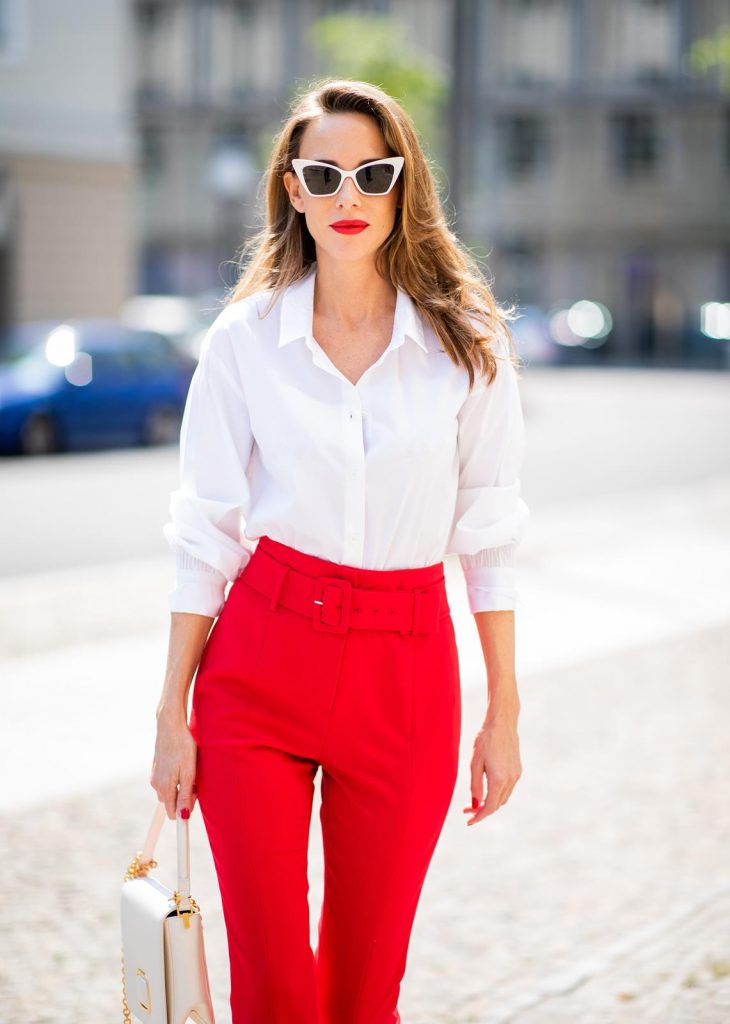 Alexandra Lapp in a Suit Style wearing a red suit combination in bright red with high waist pants with an attached belt and a slim cut blazer with an integrated waist belt, and a white shirt and a short loose knit wool coat in blue, red and white from Steffen Schraut, white snake pumps from Christian Louboutin, white and black cat-eye sunglasses by Saint Laurent and a white handbag from Roger Vivier with a golden buckle and chain seen during the Berlin Fashion Week July 2018 on July 5, 2018 in Berlin, Germany.