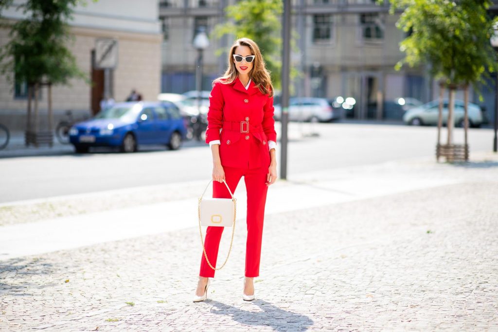 Alexandra Lapp in a Suit Style wearing a red suit combination in bright red with high waist pants with an attached belt and a slim cut blazer with an integrated waist belt, and a white shirt and a short loose knit wool coat in blue, red and white from Steffen Schraut, white snake pumps from Christian Louboutin, white and black cat-eye sunglasses by Saint Laurent and a white handbag from Roger Vivier with a golden buckle and chain seen during the Berlin Fashion Week July 2018 on July 5, 2018 in Berlin, Germany.