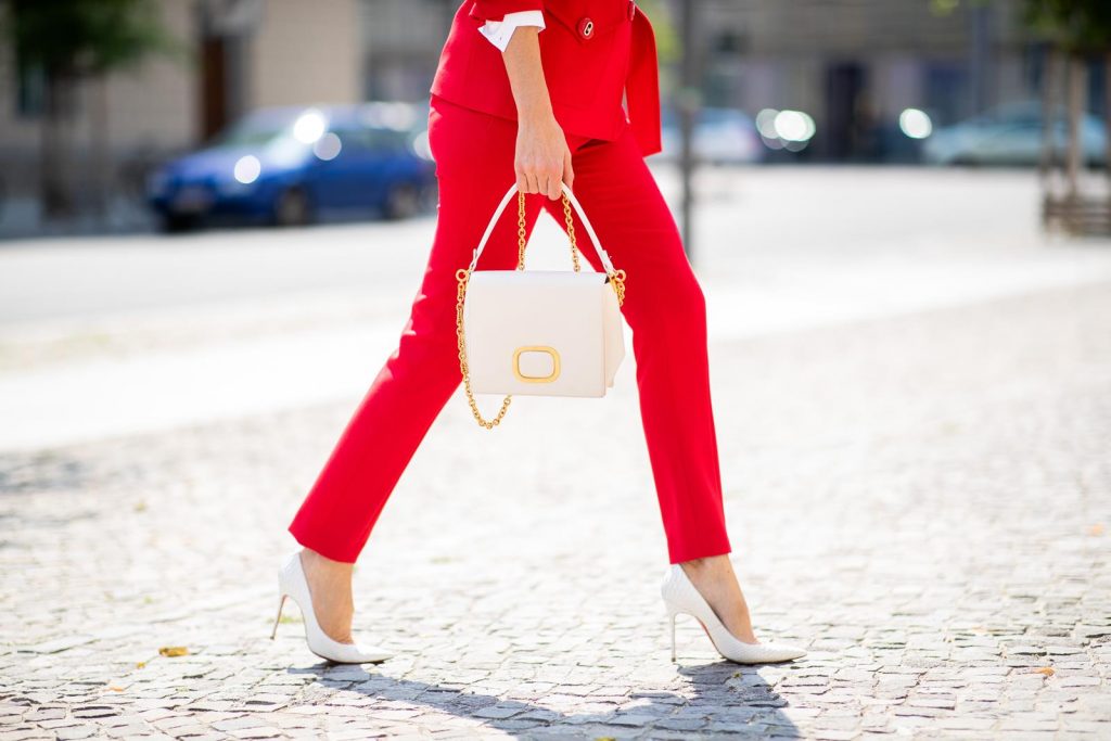 Alexandra Lapp in a Suit Style wearing a red suit combination in bright red with high waist pants with an attached belt and a slim cut blazer with an integrated waist belt, and a white shirt and a short loose knit wool coat in blue, red and white from Steffen Schraut, white snake pumps from Christian Louboutin, white and black cat-eye sunglasses by Saint Laurent and a white handbag from Roger Vivier with a golden buckle and chain seen during the Berlin Fashion Week July 2018 on July 5, 2018 in Berlin, Germany.