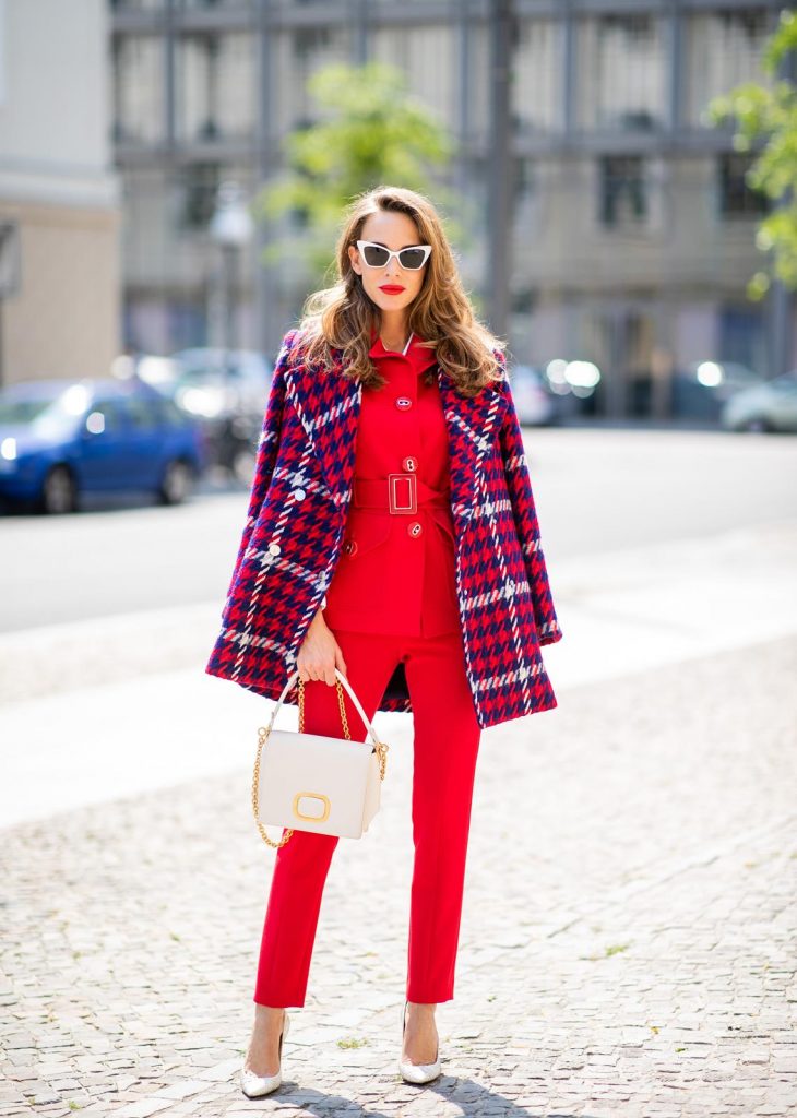 Alexandra Lapp in a Suit Style wearing a red suit combination in bright red with high waist pants with an attached belt and a slim cut blazer with an integrated waist belt, and a white shirt and a short loose knit wool coat in blue, red and white from Steffen Schraut, white snake pumps from Christian Louboutin, white and black cat-eye sunglasses by Saint Laurent and a white handbag from Roger Vivier with a golden buckle and chain seen during the Berlin Fashion Week July 2018 on July 5, 2018 in Berlin, Germany.