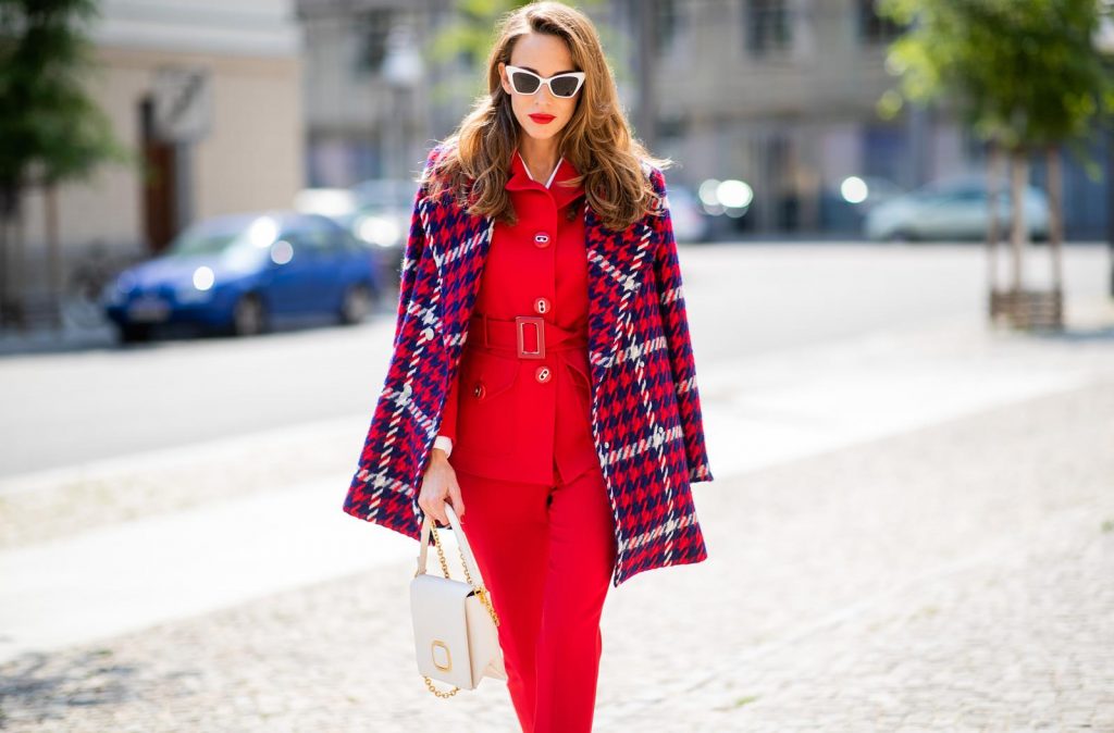 Alexandra Lapp in a Suit Style wearing a red suit combination in bright red with high waist pants with an attached belt and a slim cut blazer with an integrated waist belt, and a white shirt and a short loose knit wool coat in blue, red and white from Steffen Schraut, white snake pumps from Christian Louboutin, white and black cat-eye sunglasses by Saint Laurent and a white handbag from Roger Vivier with a golden buckle and chain seen during the Berlin Fashion Week July 2018 on July 5, 2018 in Berlin, Germany.