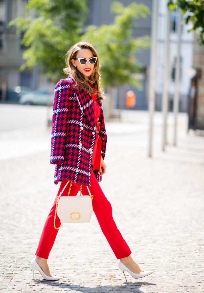 Alexandra Lapp in a Suit Style wearing a red suit combination in bright red with high waist pants with an attached belt and a slim cut blazer with an integrated waist belt, and a white shirt and a short loose knit wool coat in blue, red and white from Steffen Schraut, white snake pumps from Christian Louboutin, white and black cat-eye sunglasses by Saint Laurent and a white handbag from Roger Vivier with a golden buckle and chain seen during the Berlin Fashion Week July 2018 on July 5, 2018 in Berlin, Germany.