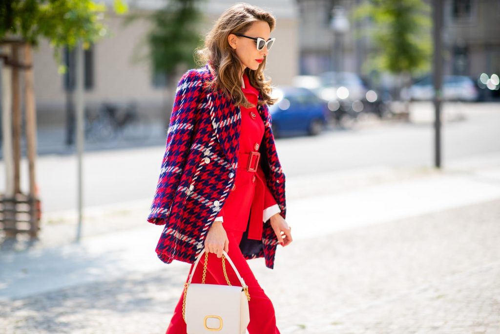 Alexandra Lapp in a Suit Style wearing a red suit combination in bright red with high waist pants with an attached belt and a slim cut blazer with an integrated waist belt, and a white shirt and a short loose knit wool coat in blue, red and white from Steffen Schraut, white snake pumps from Christian Louboutin, white and black cat-eye sunglasses by Saint Laurent and a white handbag from Roger Vivier with a golden buckle and chain seen during the Berlin Fashion Week July 2018 on July 5, 2018 in Berlin, Germany.