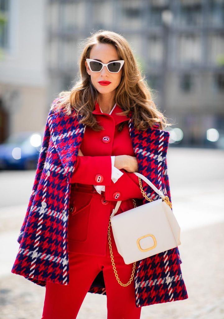 Alexandra Lapp in a Suit Style wearing a red suit combination in bright red with high waist pants with an attached belt and a slim cut blazer with an integrated waist belt, and a white shirt and a short loose knit wool coat in blue, red and white from Steffen Schraut, white snake pumps from Christian Louboutin, white and black cat-eye sunglasses by Saint Laurent and a white handbag from Roger Vivier with a golden buckle and chain seen during the Berlin Fashion Week July 2018 on July 5, 2018 in Berlin, Germany.