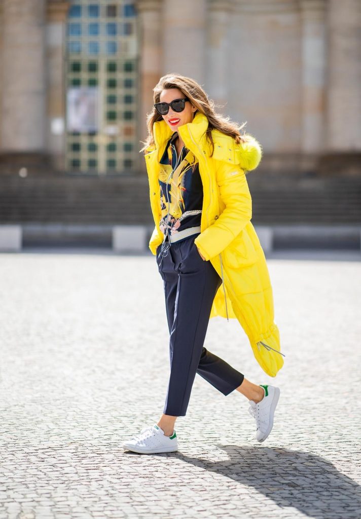 Alexandra Lapp in a Floral Jacket | Yellow Coat Look is seen wearing a blouson jacket with floral print, blue drawstring pants and a bright yellow duffle coat with a yellow fur hood from Airfield, Céline sunglasses in black, white Stan Smith Adidas sneakers with green details during the Berlin Fashion Week July 2018 on July 6, 2018 in Berlin, Germany.