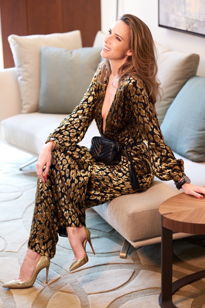 Model and Blogger Alexandra Lapp in an Animal Print Look wearing a leopard patterned jumpsuit in gold metallic by Maison Valentino, the Lou Camera Leather Crossbody Bag in black from Saint Laurent, Pigalle Follies 100 metallic crinkled leather Pumps in gold by Christian Louboutin and the Portugieser Chronograph watch by IWC.