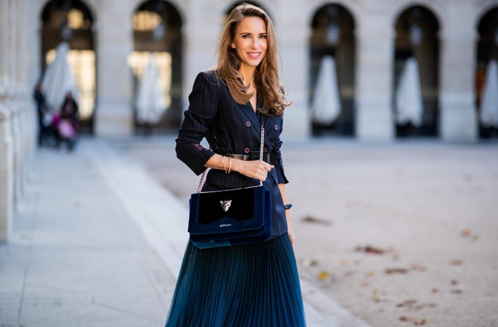 Alexandra Lapp in an All Blue Everything Look wearing a blue pleated skirt, navy striped blazer with belt and blue velvet bag all by Marc Cain, black heels from Christian Louboutin, a black lacquer waist belt by Dolce & Gabbana and black Audrey sunglasses by Céline seen during Paris Fashion Week Womenswear Spring/Summer 2019 on September 25, 2018 in Paris, France.