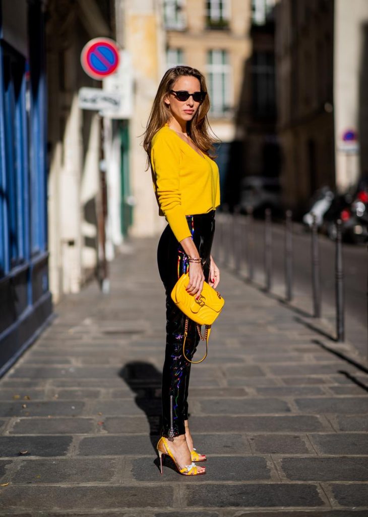Alexandra Lapp in a Vinyl Pants Look wearing black zipped patent leather trousers from Balmain, a yellow v-neck knit jumper by Allude, shiny black down jacket by Ahirain, yellow Gucci Matelasse GG bag, yellow white Metrisandal open toe sandals with tape-style straps by Christian Louboutin and cat-eye shaped Isabella Sunglasses by illesteva during Paris Fashion Week Womenswear Spring/Summer 2019 on September 27, 2018 in Paris, France.