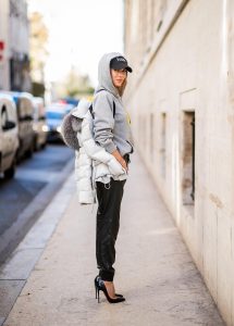 Alexandra Lapp in a Light Down Jacket Look wearing a light grey, fitted down jacket with inner carriers by Airfield, a handmade grey Hoodie with hand-painted print by Wodka Ogurez, black leather pants by SET, black Femme baseball cap from Balenciaga and black patent leather pumps by Christian Louboutin during Paris Fashion Week Womenswear Spring/Summer 2019 on September 24, 2018 in Paris, France.