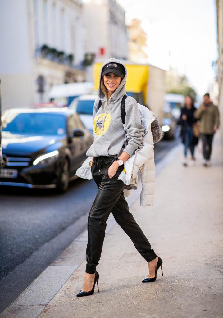 Alexandra Lapp in a Light Down Jacket Look wearing a light grey, fitted down jacket with inner carriers by Airfield, a handmade grey Hoodie with hand-painted print by Wodka Ogurez, black leather pants by SET, black Femme baseball cap from Balenciaga and black patent leather pumps by Christian Louboutin during Paris Fashion Week Womenswear Spring/Summer 2019 on September 24, 2018 in Paris, France.