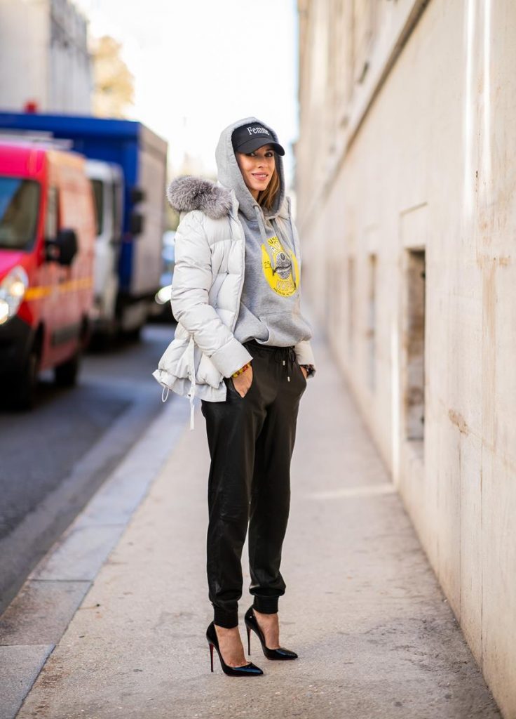 Alexandra Lapp in a Light Down Jacket Look wearing a light grey, fitted down jacket with inner carriers by Airfield, a handmade grey Hoodie with hand-painted print by Wodka Ogurez, black leather pants by SET, black Femme baseball cap from Balenciaga and black patent leather pumps by Christian Louboutin during Paris Fashion Week Womenswear Spring/Summer 2019 on September 24, 2018 in Paris, France.