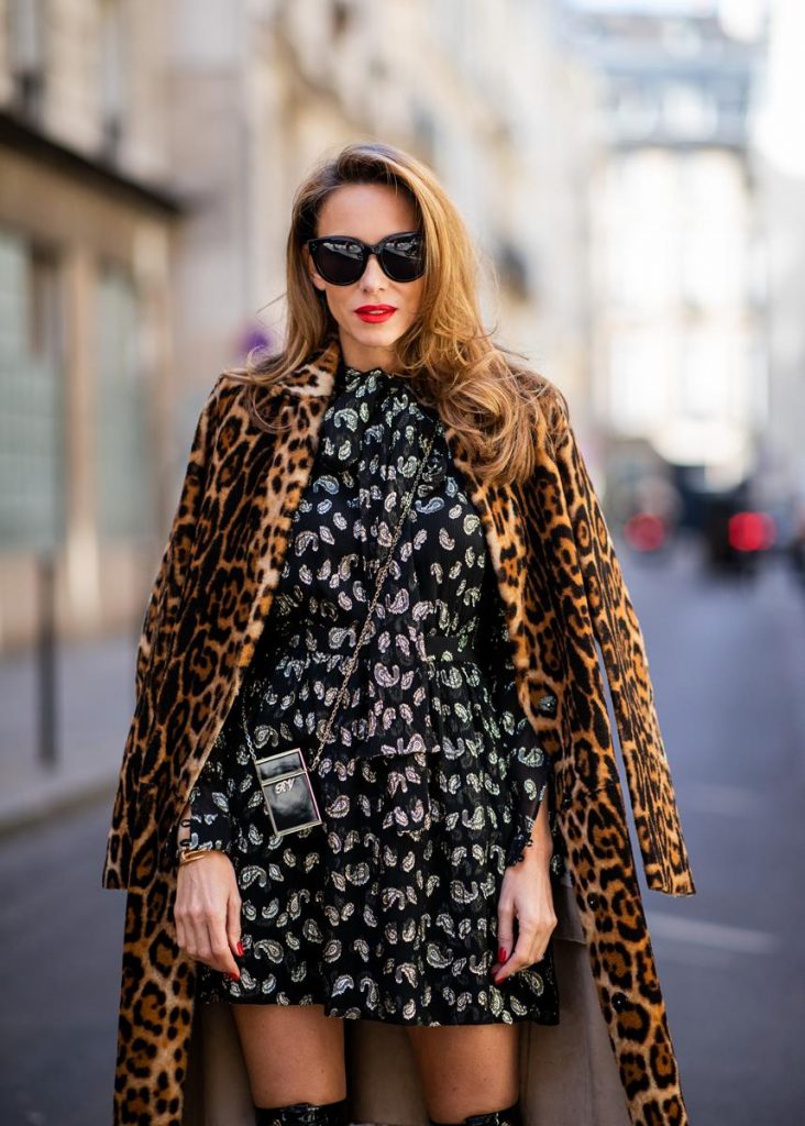 Alexandra Lapp in a Saint Laurent dress Look wearing a glitter paisley patterned dress by Saint Laurent, a reversible Shearling Trench Coat in a leopard look by Yves Salomon, Frenchissima Alta Overknees in patent soft black leather by Christian Louboutin, a Roger Vivier Stars Rivets leather cigarette case with a long golden chain and black Audrey sunglasses by Celine is seen during Paris Fashion Week Womenswear Spring/Summer 2019 on October 1, 2018 in Paris, France.