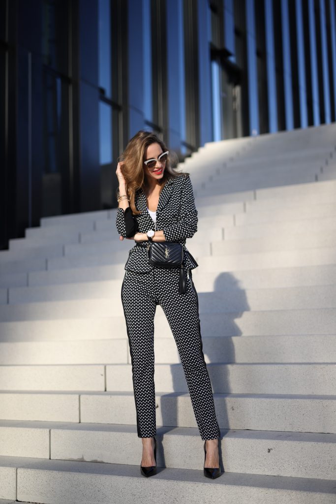 Alexandra Lapp in a Businesswoman Look wearing blazer and pants with polka dots in black white both from Airfield, red Jadicted silk top, black Lou leather belt bag by Saint Laurent, black patent leather pumps by Christian Louboutin, a black bakerboy cap by Dior and cat-eyed shaped vintage Gucci sunglasses with a white rim. 