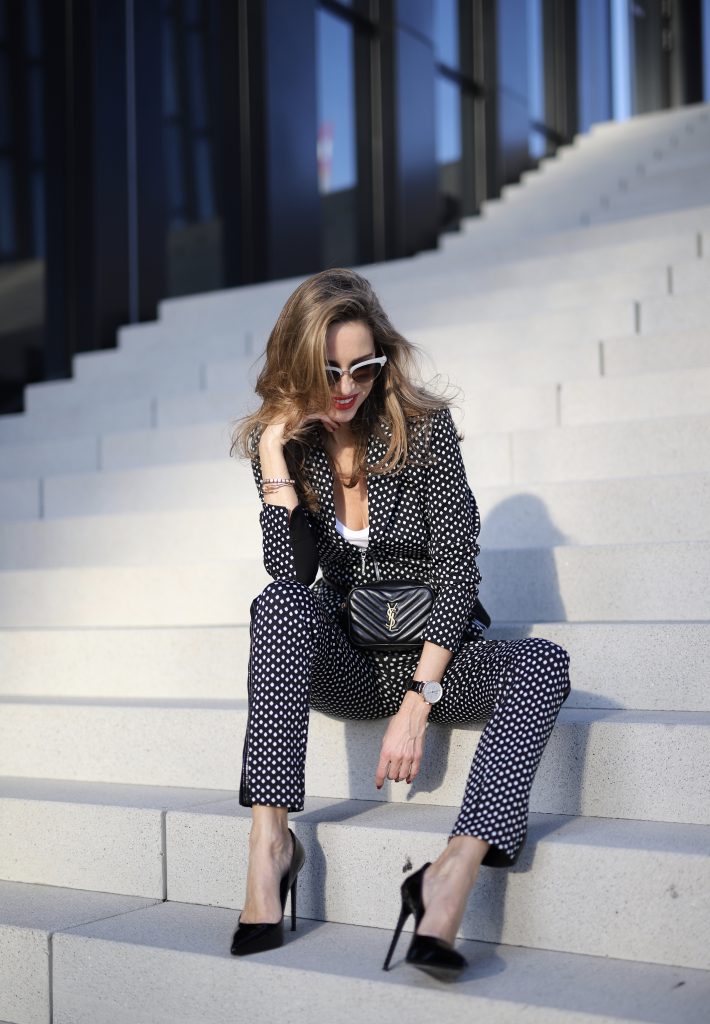 Alexandra Lapp in a Businesswoman Look wearing blazer and pants with polka dots in black white both from Airfield, red Jadicted silk top, black Lou leather belt bag by Saint Laurent, black patent leather pumps by Christian Louboutin, a black bakerboy cap by Dior and cat-eyed shaped vintage Gucci sunglasses with a white rim. 