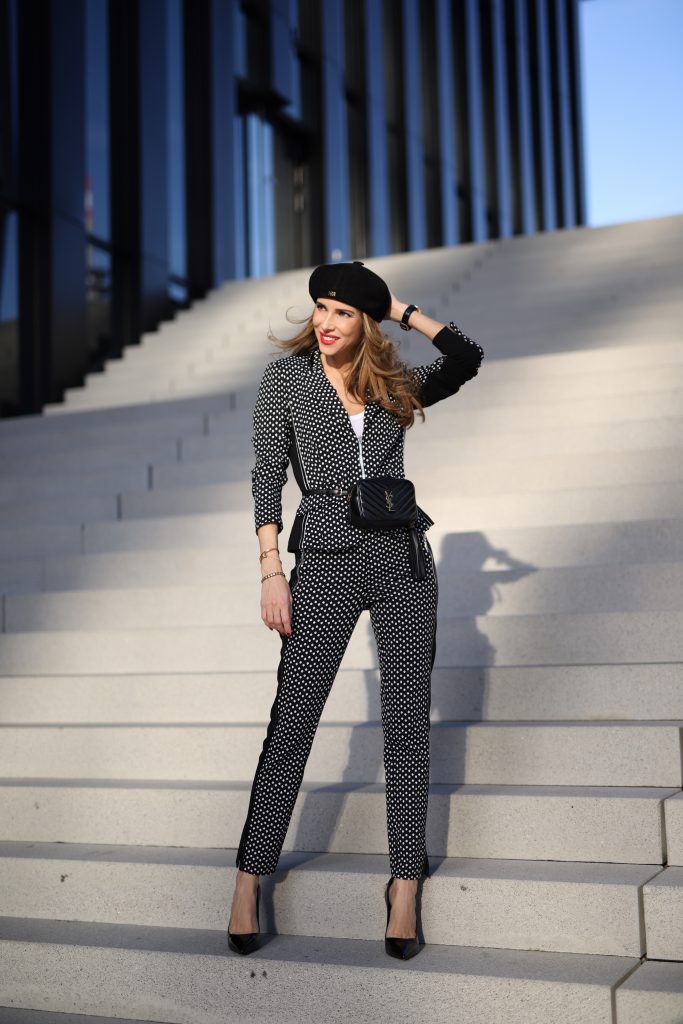 Alexandra Lapp in a Businesswoman Look wearing blazer and pants with polka dots in black white both from Airfield, red Jadicted silk top, black Lou leather belt bag by Saint Laurent, black patent leather pumps by Christian Louboutin, a black bakerboy cap by Dior and cat-eyed shaped vintage Gucci sunglasses with a white rim. 