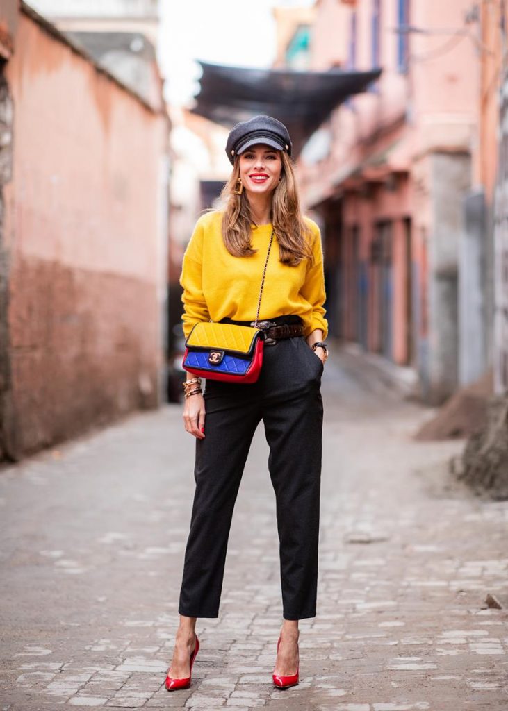 Alexandra Lapp in a Yellow Knit look, wearing a yellow crew-neck cashmere sweater from Jardin des Orangers, high-waisted trousers in dark grey by H&M, Graphic Flap Bag from Chanel in black/red/yellow/blue, brown lacquer Kieselstein Cord Crocodile belt, red lacquer pumps from Gianvito Rossi and dark grey nautical cap with buttons by ZARA on November 25, 2018 in Marrakech, Morocco.