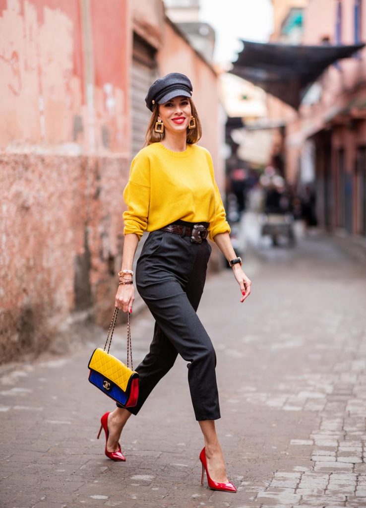 Alexandra Lapp in a Yellow Knit look, wearing a yellow crew-neck cashmere sweater from Jardin des Orangers, high-waisted trousers in dark grey by H&M, Graphic Flap Bag from Chanel in black/red/yellow/blue, brown lacquer Kieselstein Cord Crocodile belt, red lacquer pumps from Gianvito Rossi and dark grey nautical cap with buttons by ZARA on November 25, 2018 in Marrakech, Morocco.