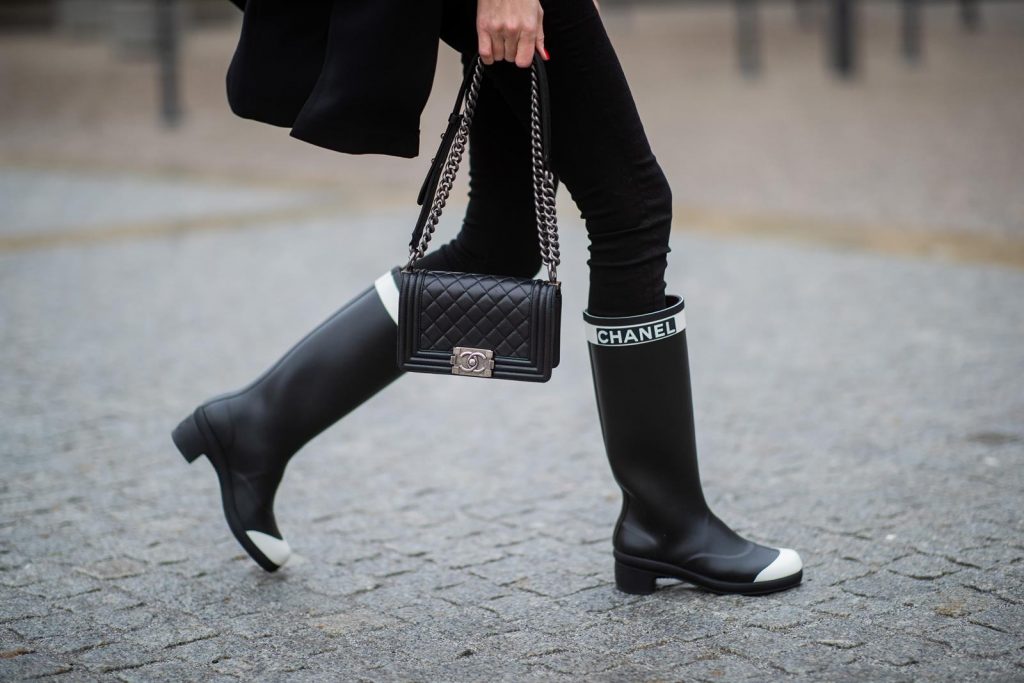 Alexandra Lapp in A Chanel Rain Boots look, wearing a soft long blazer by Steffen Schraut, over a white chunky knit sweater by H&M, black skinny pants with golden buttons by Veronica Beard, styled with Chanel logo suspenders and Chanel rain boots, the Chanel Le boy bag, a Chanel tweed baker boy cap and a transparent umbrella by Mirviory during the Berlin Fashion Week Autumn/Winter 2019 on January 15, 2019 in Berlin, Germany. (Photo by Christian Vierig/Getty Images)