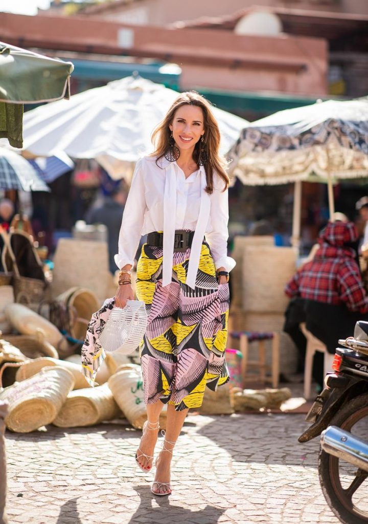 Alexandra Lapp in a Le Riad look, wearing a flared skirt printed with pink, yellow and black patterns combined with a plain bowed white shirt, a matching silk printed scarf with elephants in the same colours and round big earrings in black all by Marc Cain, leather sandals in white, white bag and black cat-eyed shaped sunglasses on November 25, 2018 in Marrakech, Morocco. (Photo by Christian Vierig/Getty Images)