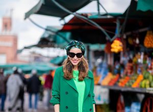 Alexandra Lapp in a Le Riad look, wearing a belted long crepe Marc Cain coat in green, a neon green sweater and crepe loose-fit pants with stripes in two green tones by Marc Cain, a black small trapeze shaped bag and a printed silk scarf in multi green shades by Marc Cain, black lacquer high heels, black sunglasses and round oversized earrings in black by Marc Cain on November 26, 2018 in Marrakech, Morocco.