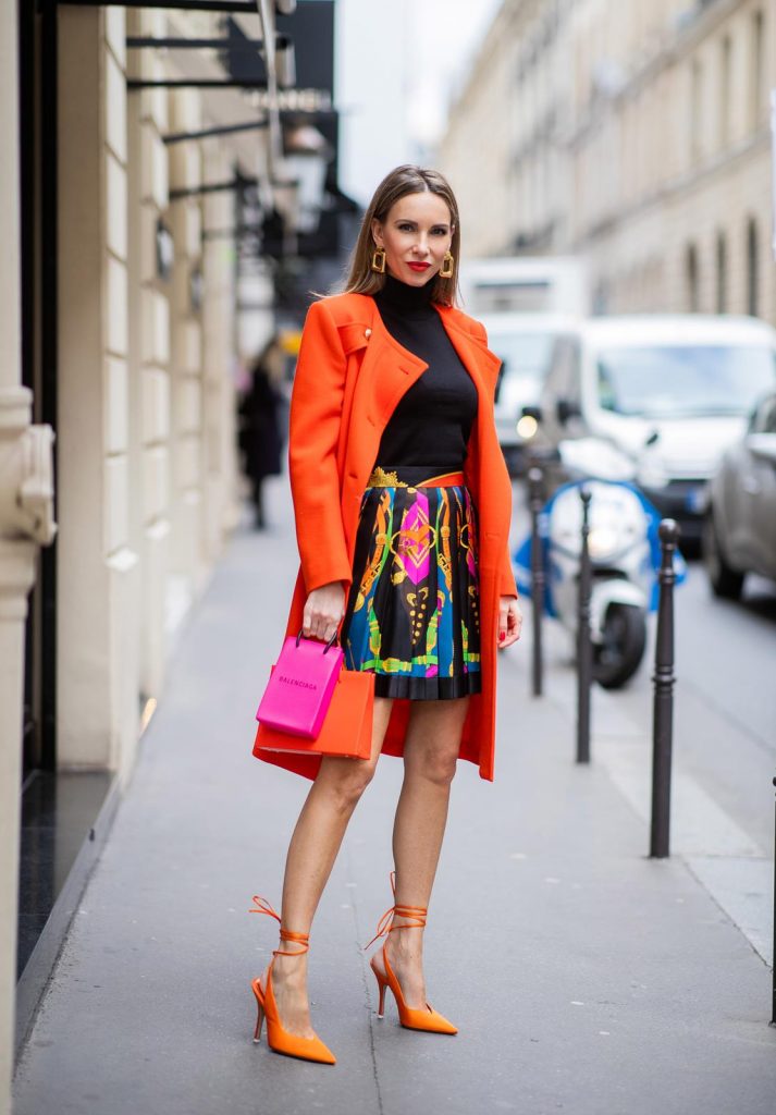 PARIS, FRANCE - FEBRUARY 26: Alexandra Lapp is seen wearing a Givenchy coat in orange, pleated silk skirt from Versace, turtleneck pullover in black from Dorothee Schumacher, slingback pumps in orange from The Attico, Balenciaga Tote Shopping Phone bag, Medea Vinile Short bag during Paris Fashion Week - Womenswear Fall/Winter 2020/2021 : Day Three on February 26, 2020 in Paris, France.