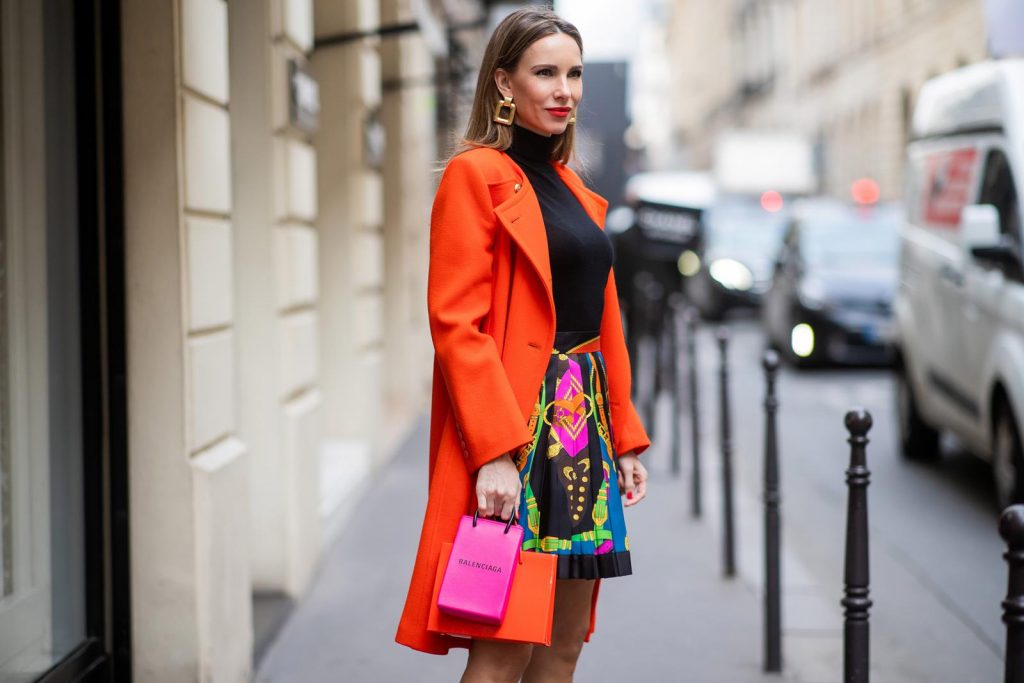 PARIS, FRANCE - FEBRUARY 26: Alexandra Lapp is seen wearing a Givenchy coat in orange, pleated silk skirt from Versace, turtleneck pullover in black from Dorothee Schumacher, slingback pumps in orange from The Attico, Balenciaga Tote Shopping Phone bag, Medea Vinile Short bag during Paris Fashion Week - Womenswear Fall/Winter 2020/2021 : Day Three on February 26, 2020 in Paris, France.