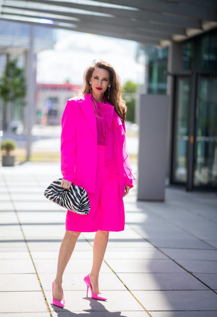 Alexandra Lapp is seen wearing pink blazer by Valentino, shorts and Valentino silk blouse with a bow - all in pink, Square Knife pumps in neon pink from Balenciaga, Saint Laurent earrings with a heart and YSL letters and Bottega Veneta Clutch The Pouch with Zebra pattern all styles from Breuninger.