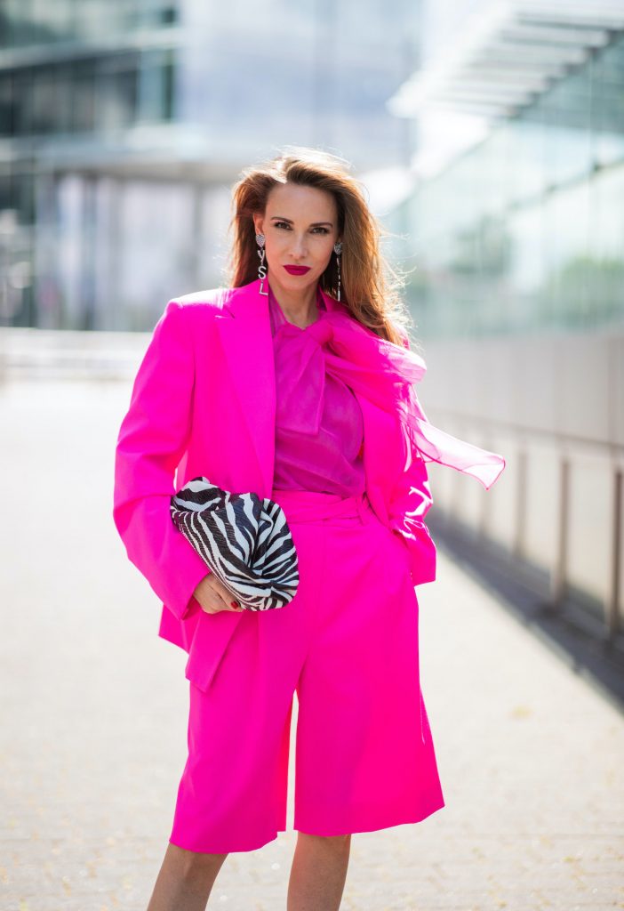 Alexandra Lapp is seen wearing pink blazer by Valentino, shorts and Valentino silk blouse with a bow - all in pink, Square Knife pumps in neon pink from Balenciaga, Saint Laurent earrings with a heart and YSL letters and Bottega Veneta Clutch The Pouch with Zebra pattern all styles from Breuninger.