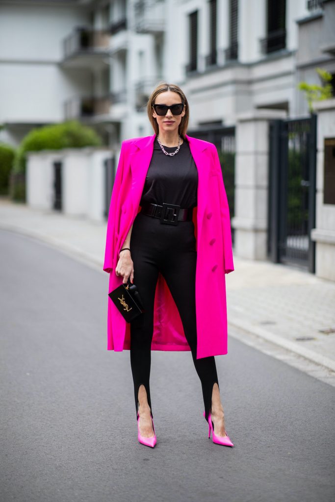 Alexandra Lapp is seen wearing Saint Laurent stretch knit stirrup leggings in black, black oversize t-shirt with shoulder pads from H&M, Dolce Gabbana waist belt in black, Square Knife pumps in neon pink from Balenciaga, double breasted oversize coat and pink blazer from The Attico in pink, Saint Laurent Monogram Clutch in black and Tiffany City HardWear necklace in sterling silver.