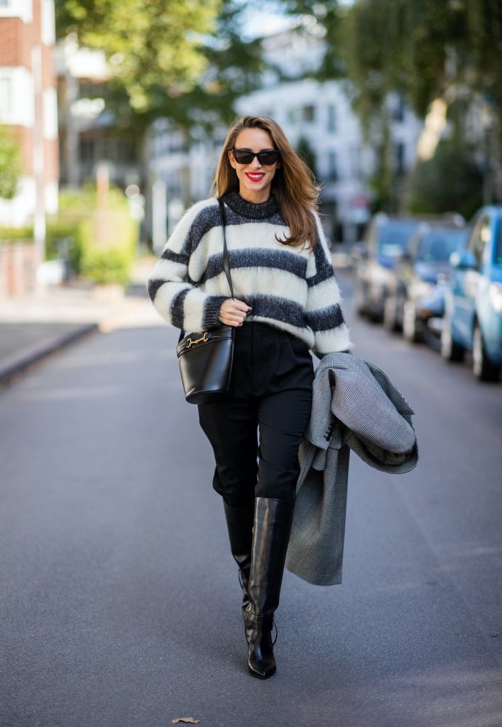 Alexandra Lapp is seen wearing Alexander McQueen coat with prince of wales check, SAINT LAURENT striped mohair-blend sweater, SAINT LAURENT high waist pants in black, CELINE Bucket Crécy bag in black and Isabel Marant pointed-toe knee-high autumn boots in black. All looks by Breuninger.