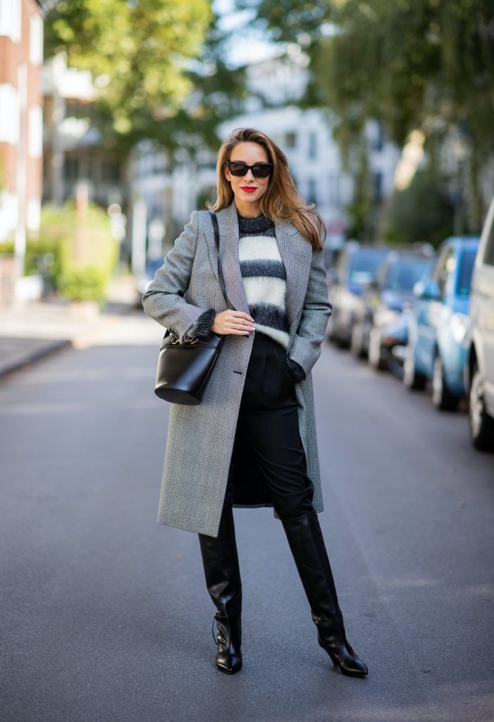 Alexandra Lapp is seen wearing Alexander McQueen coat with prince of wales check, SAINT LAURENT striped mohair-blend sweater, SAINT LAURENT high waist pants in black, CELINE Bucket Crécy bag in black and Isabel Marant pointed-toe knee-high autumn boots in black. All looks by Breuninger.