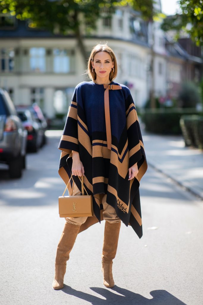 Alexandra Lapp is seen wearing Chloé striped wool cape, Chloé chunky-knit sleeveless jumper in camel, Chloé linen cargo pants in beige, SAINT LAURENT Kate medium bag in camel and CELINE Claude calfskin autumn boots in sand. All looks by Breuninger.