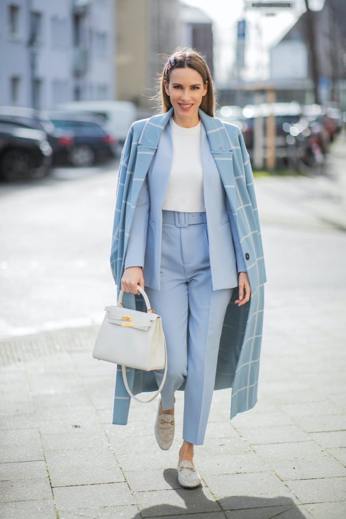 Alexandra Lapp is seen wearing pastel suits from ZARA checked coat in ligth blue, ZARA blazer in pastel blue, ZARA knit jumper in white, ZARA pants in pastel blue, GUCCI hair clips, HERMÈS Kelly 28 bag in white, GUCCI loafers in silver and white