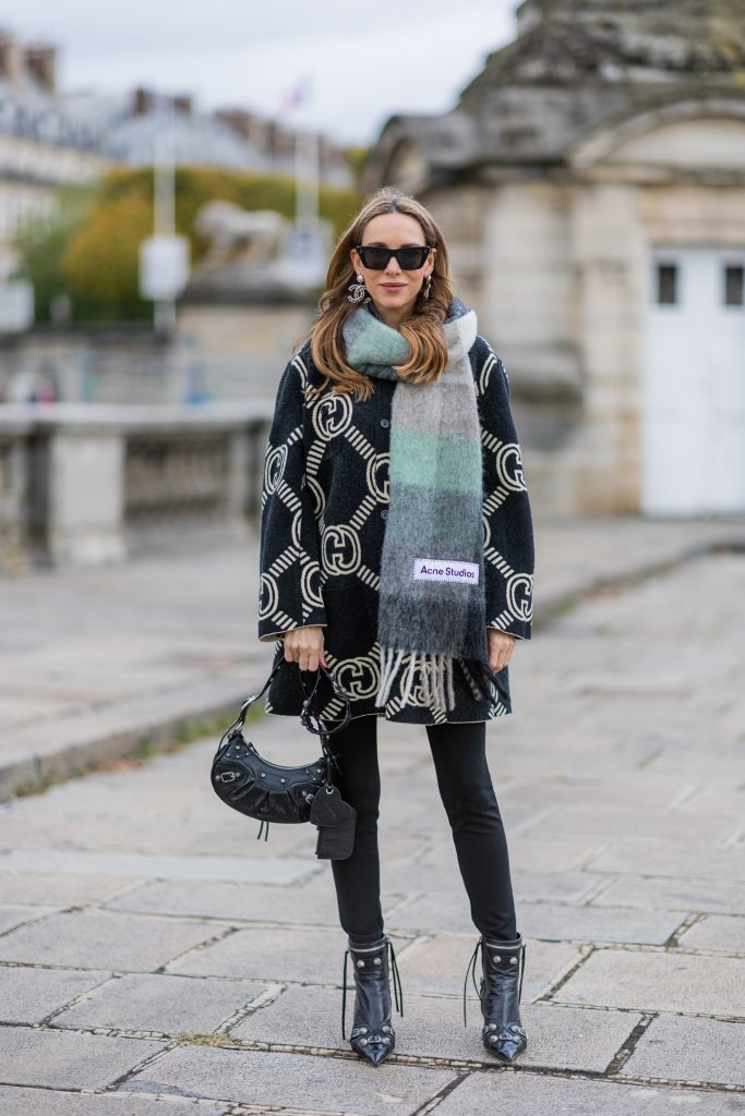 Alexandra Lapp is seen wearing GUCCI reversible cardigan in black and ecru, BALMAIN pants in black, ACNE STUDIOS scarf in green and grey, BALENCIAGA Le Cagole bag in black, BALENCIAGA ankle boots Cagole in black, CELINE cat eye sunglasses in silver, and Chanel ear rings in black. 