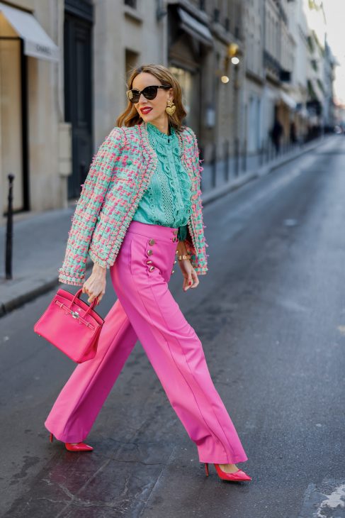 Alexandra Lapp is seen wearing colorful look during Paris Fashion Week by MAISON COMMON tweed jacket in green and pink, MAISON COMMON ruffles blouse in green, MAISON COMMON flared trousers in pink, ZARA heart ear rings in gold, HERMES Kelly bag in pink, and PRADA pumps in pink.